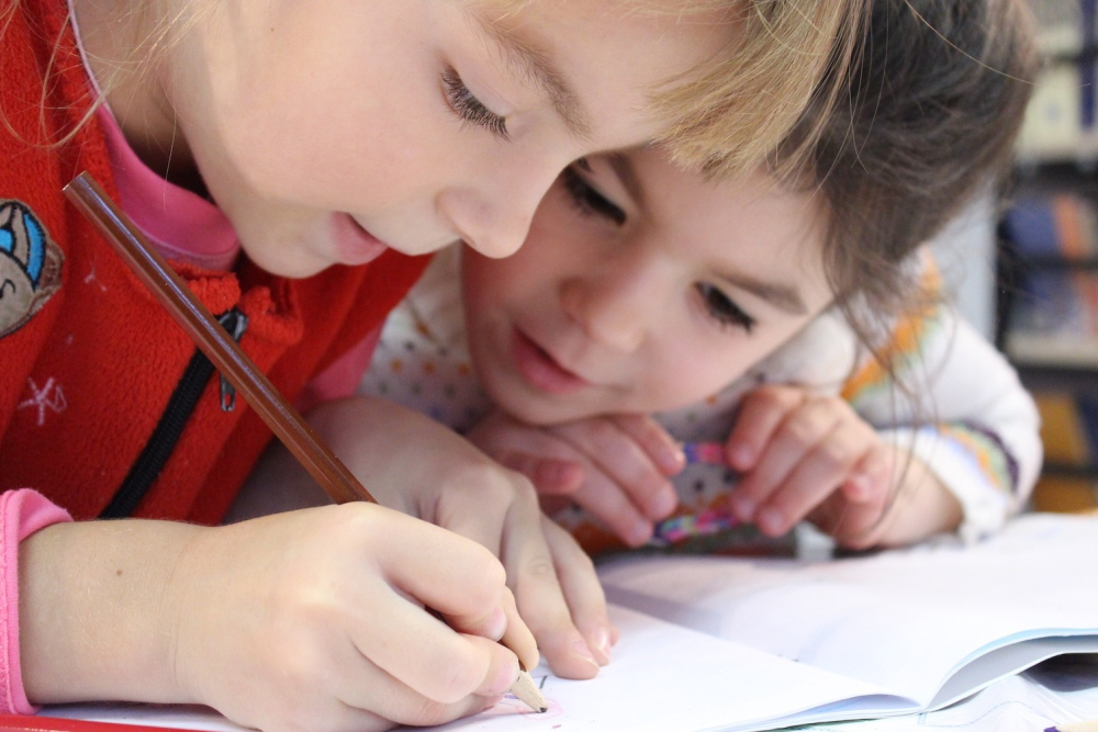 Two children using pencil to draw on a paper